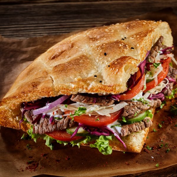 A doner kebab with appetizing meat and fresh vegetables placed on a table