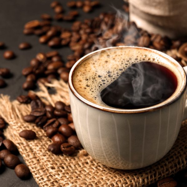 Cup of aromatic hot coffee and beans on black table, closeup